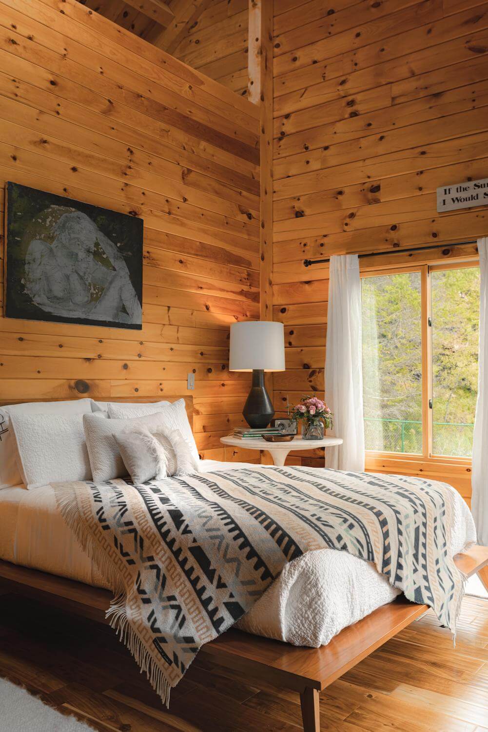 Wooden cabin bedroom with a bed, lamp, and window view.