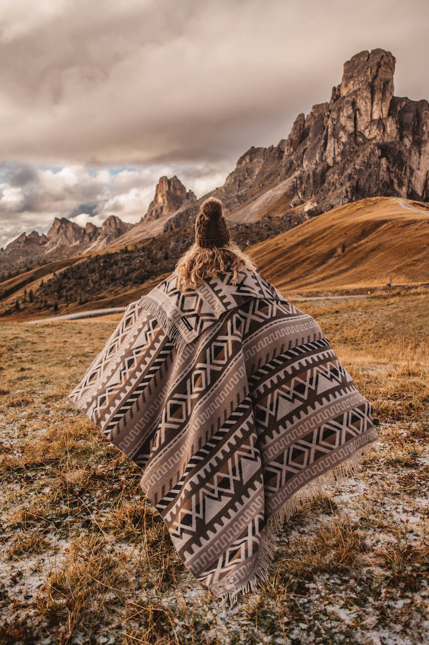 Person wrapped in a patterned blanket standing in a mountainous landscape