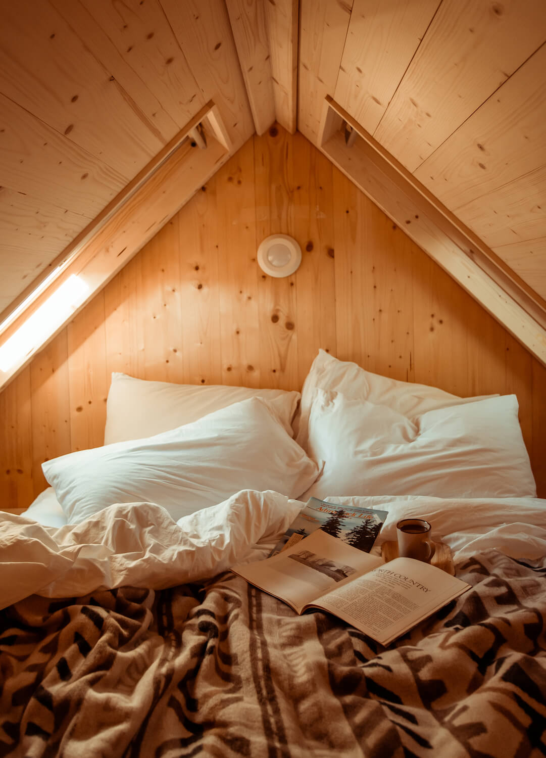 Bed with white pillows and brown blanket in a wooden attic room