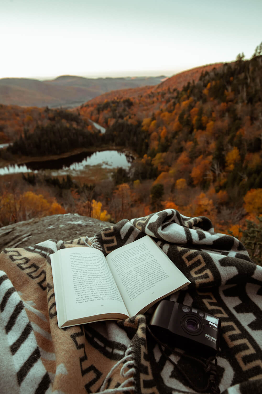 Open book on a patterned blanket with a scenic view of mountains and trees in the background