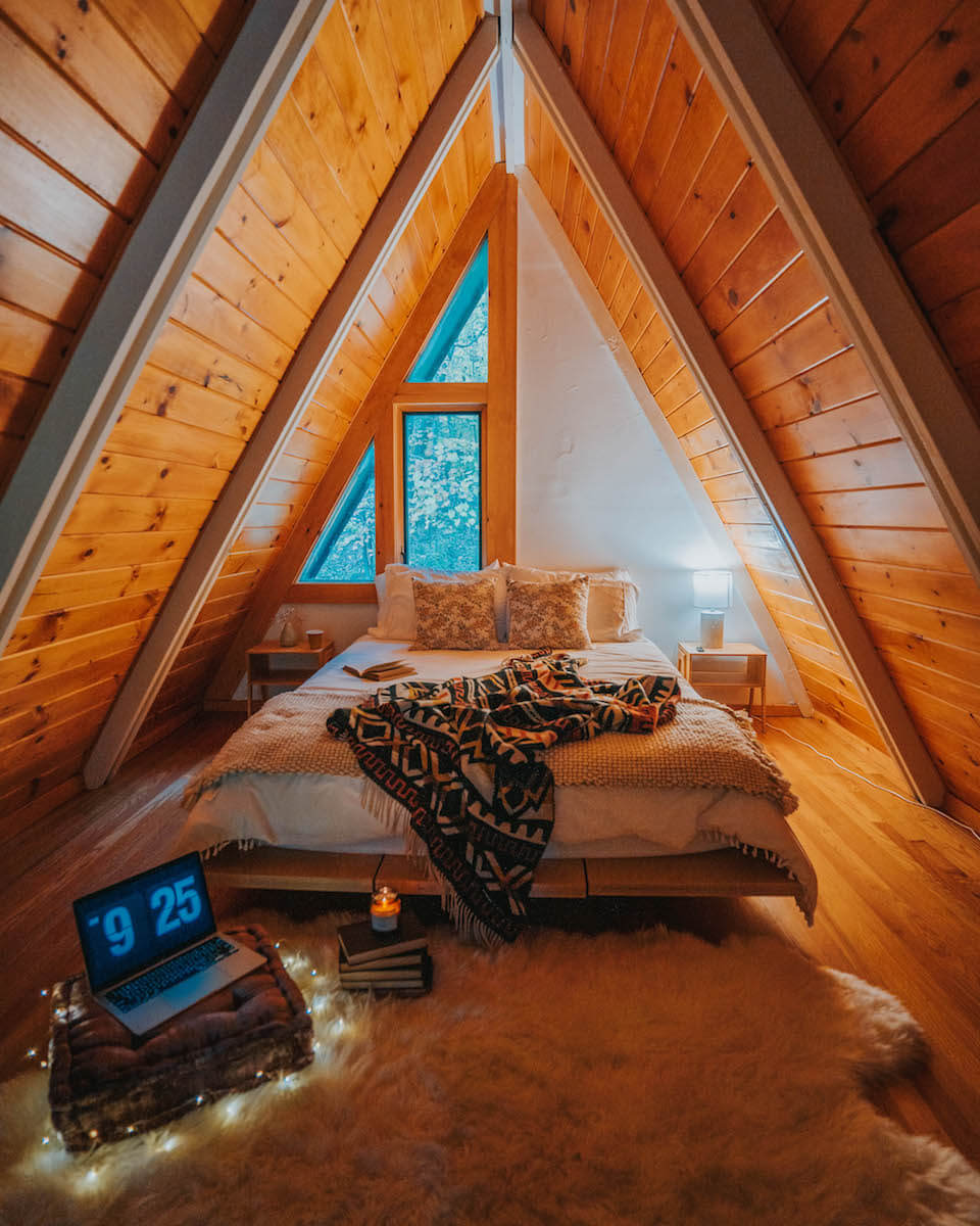 Cozy bedroom with wooden walls, a bed, and a laptop on a crate.