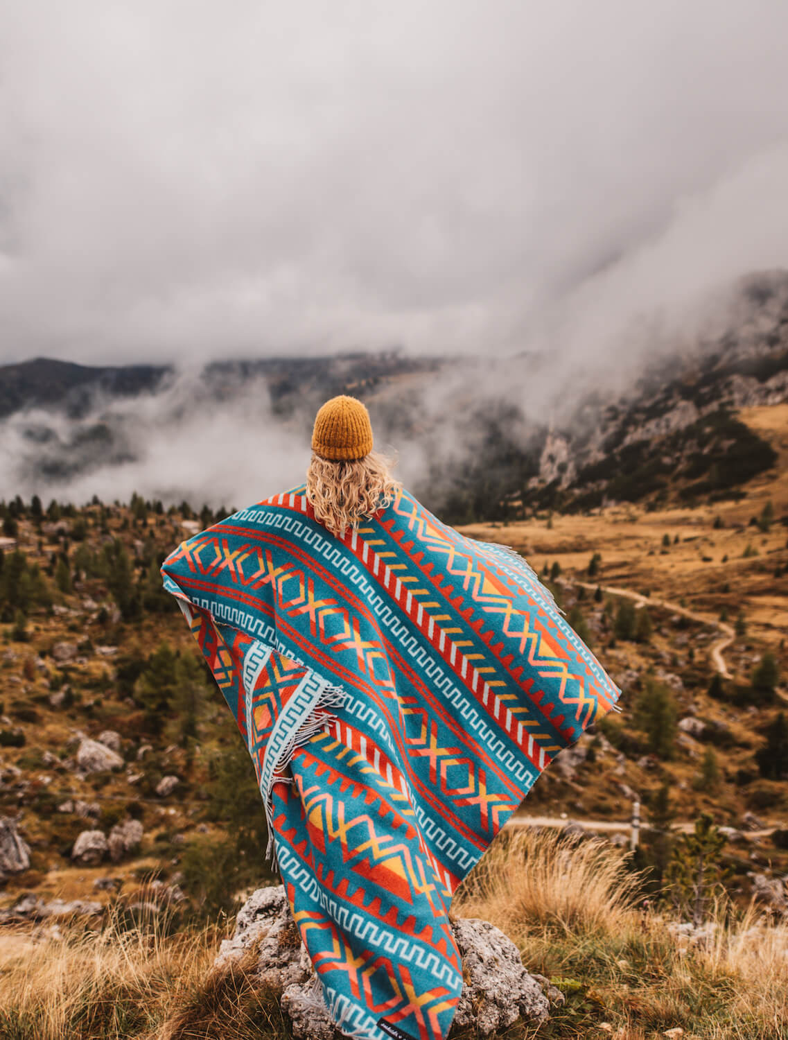 Person wrapped in a colorful patterned blanket overlooking misty mountains