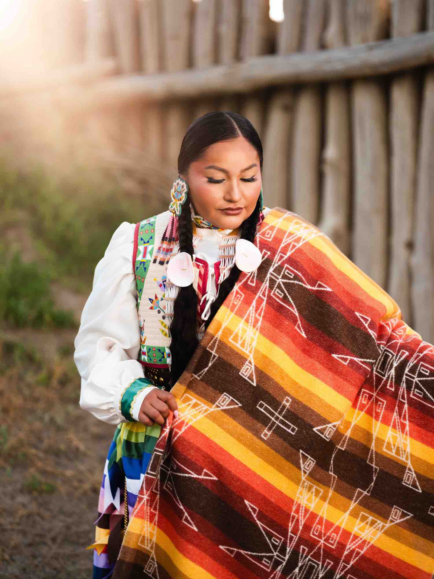 Person wearing a colorful patterned blanket with a wooden fence in the background