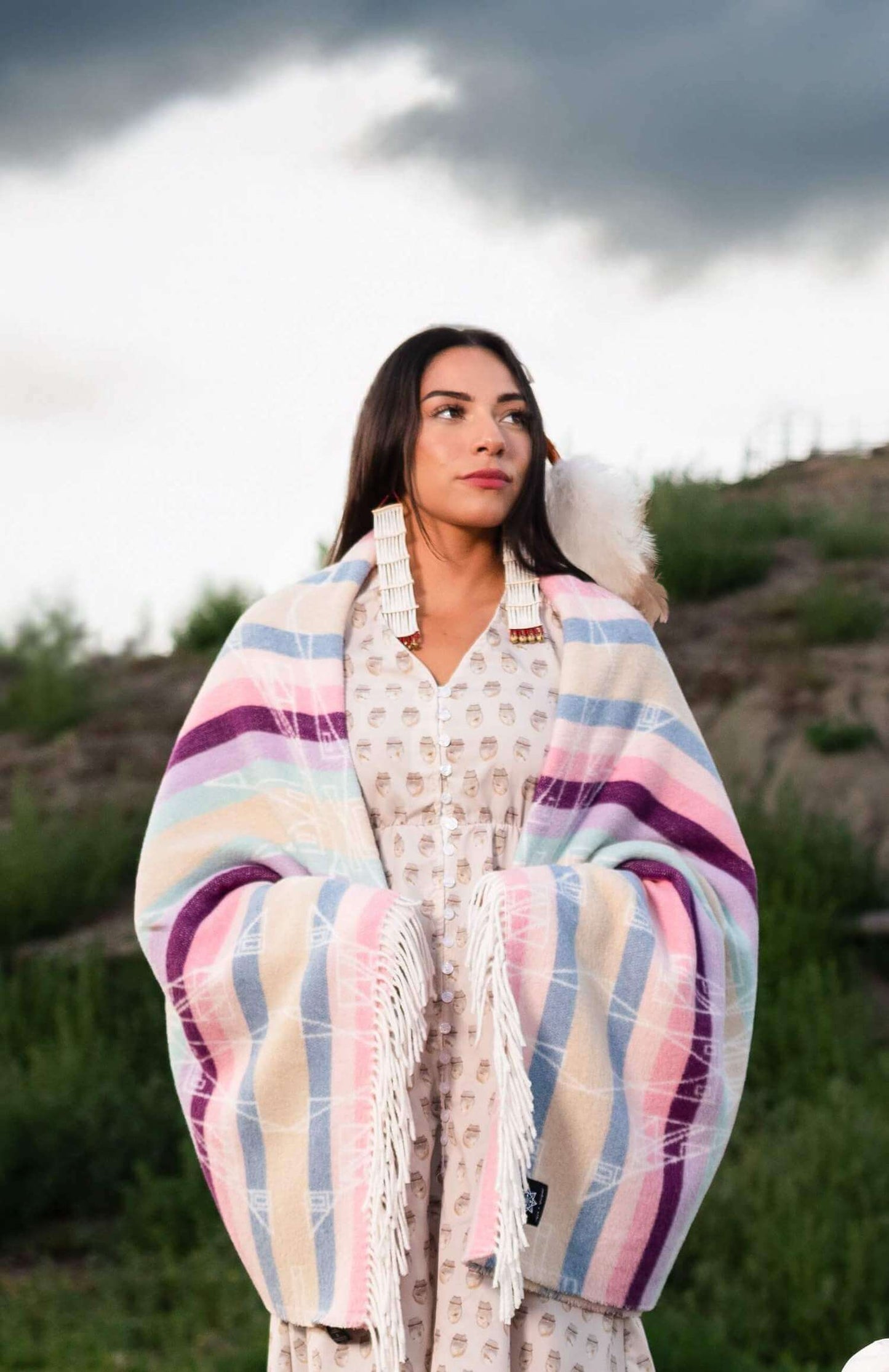 Woman wrapped in a colorful striped blanket outdoors with a scenic background