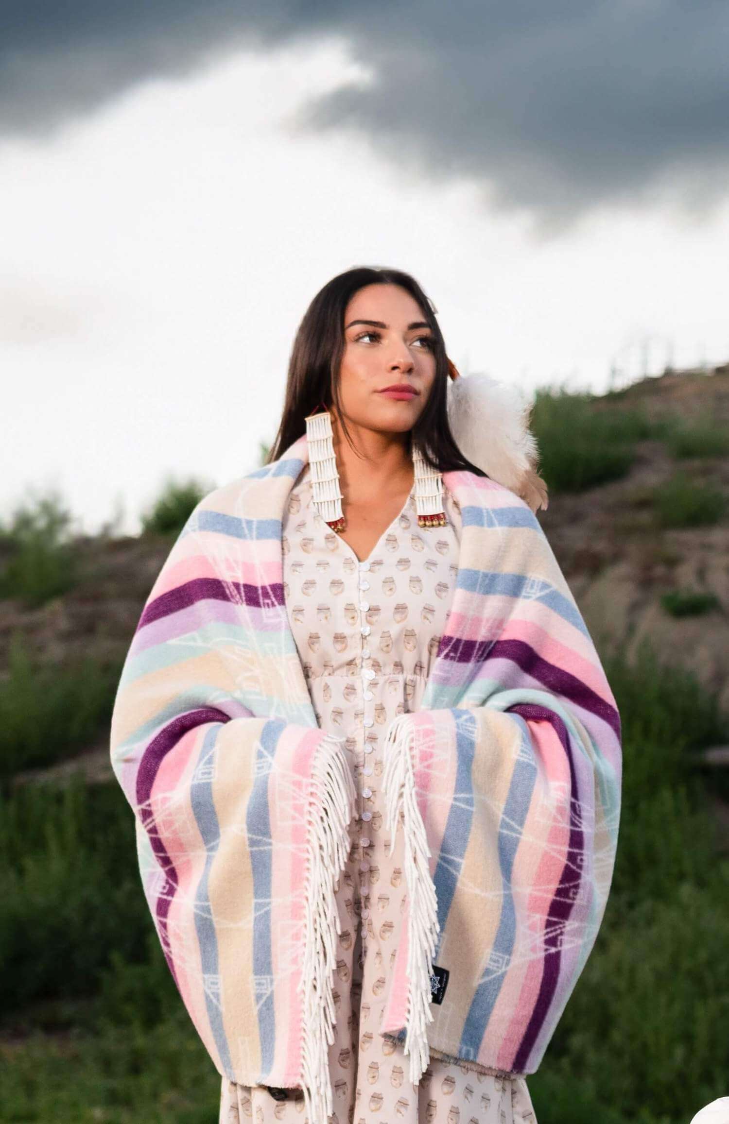 Woman wrapped in a colorful striped blanket outdoors with a scenic background