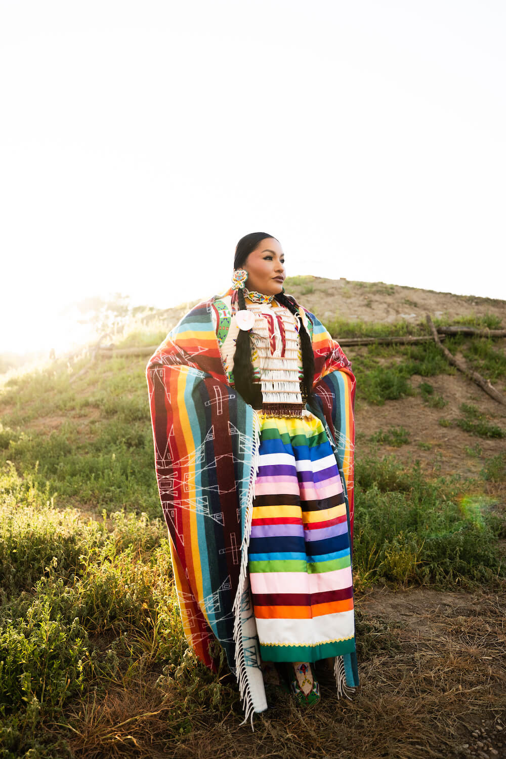 Person wearing a colorful traditional outfit with a rainbow pattern in a natural setting.