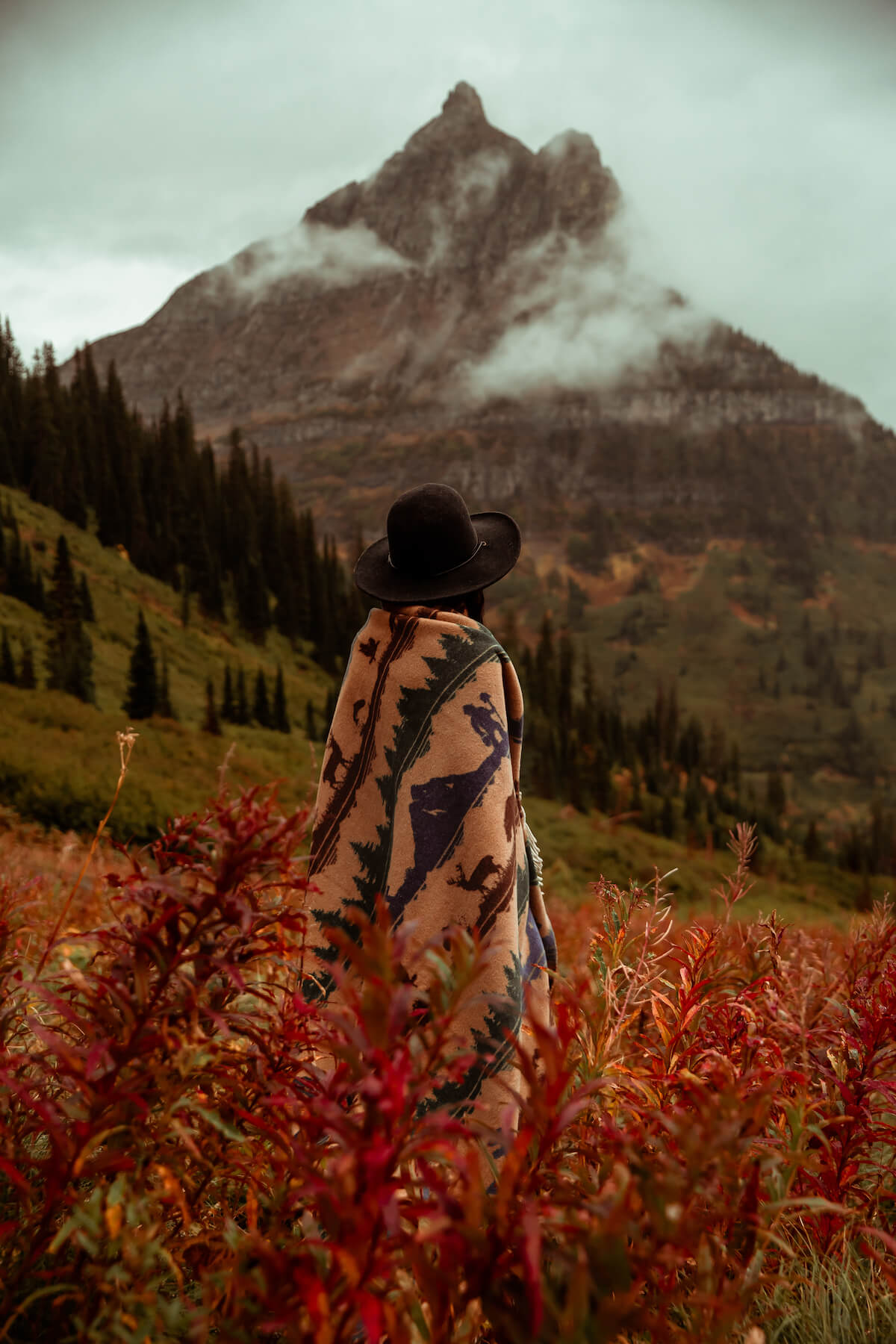 Person wrapped in a patterned blanket standing in a field with a mountain in the background