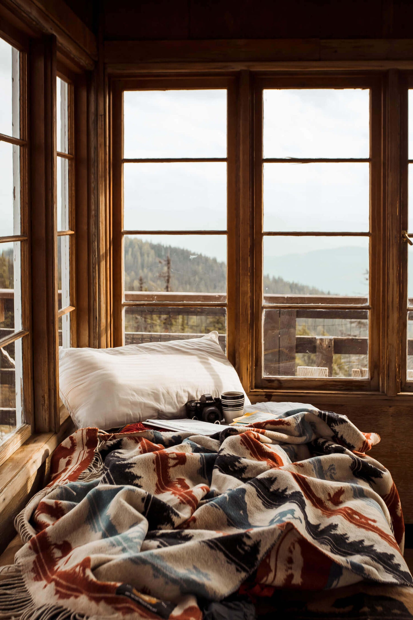 Bed with patterned blanket and pillows in a room with large windows overlooking a scenic view.
