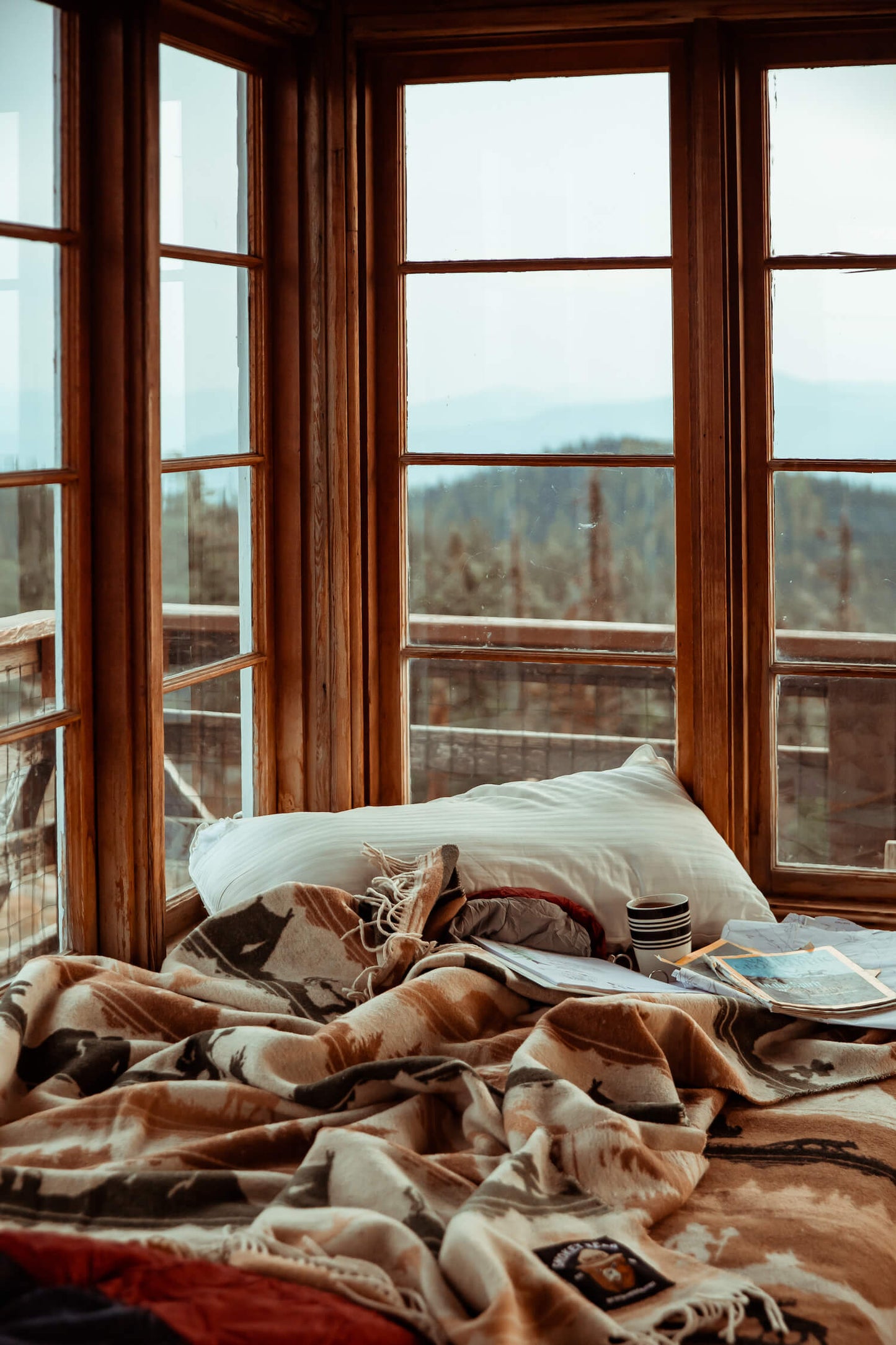 Bed with pillows and blankets in a room with large windows overlooking a scenic view.