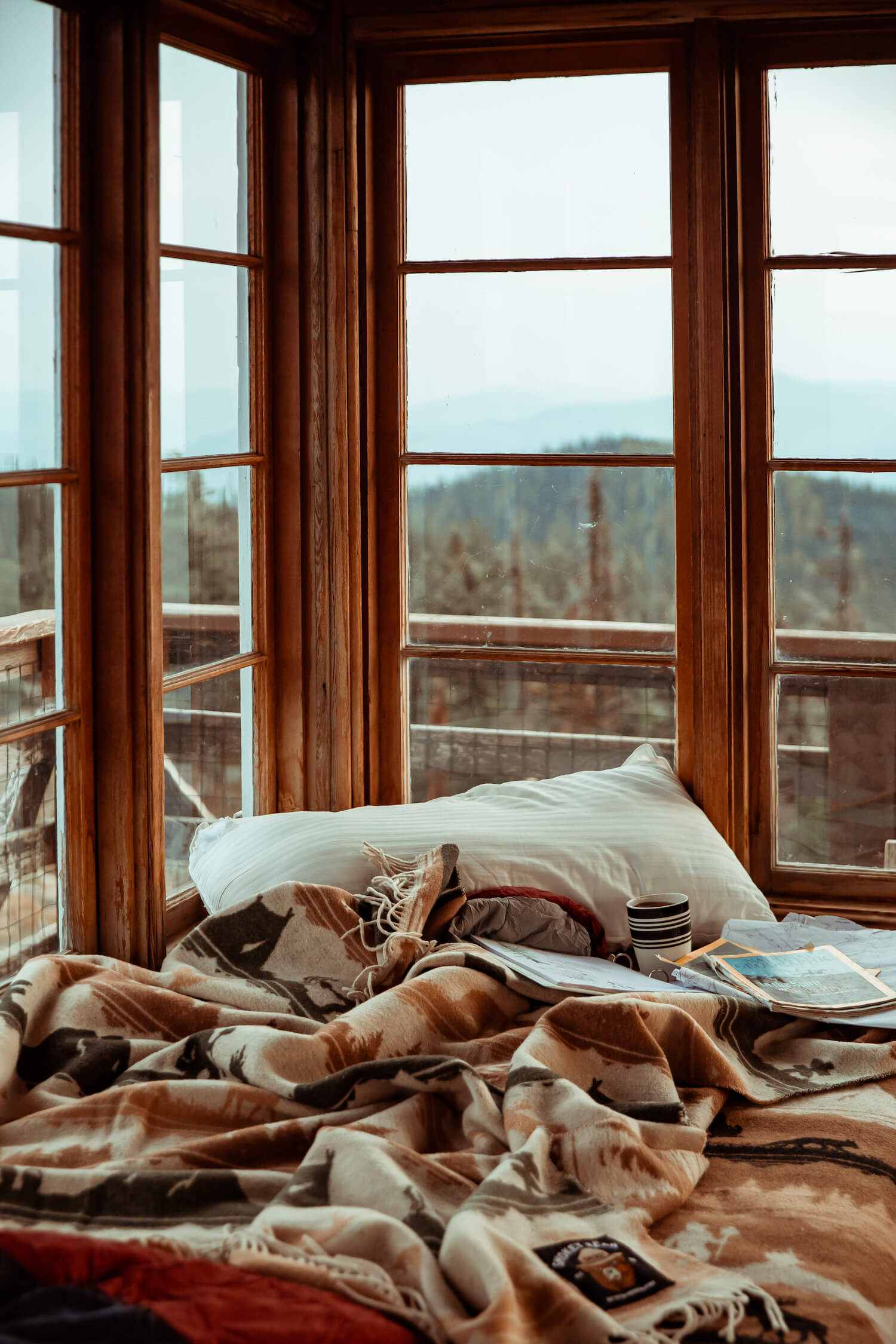 Bed with pillows and blankets in a room with large windows overlooking a scenic view.