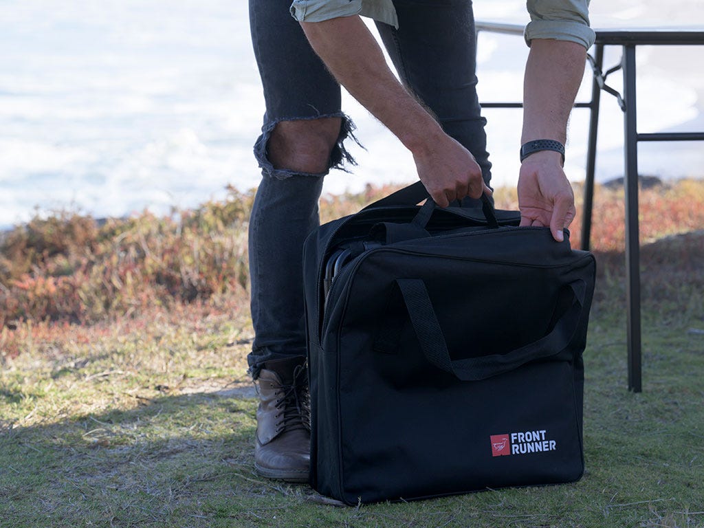 Person holding a black bag with 'Front Runner' logo outdoors.