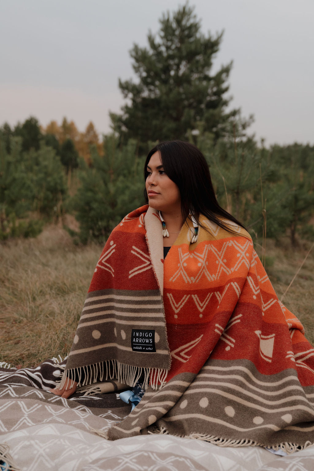Woman sitting outdoors under a patterned blanket with trees in the background
