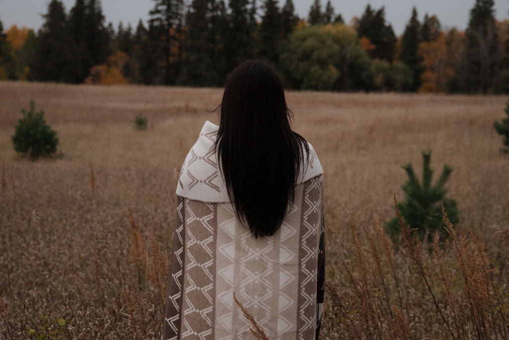 Person wrapped in a patterned blanket standing in a field with trees in the background