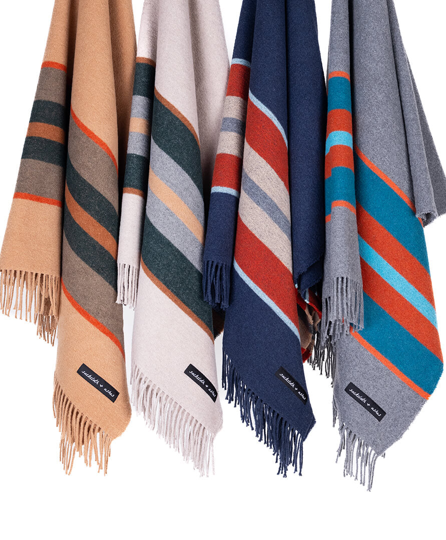 Four striped blankets in beige, white, blue, and gray with fringes on a white background.