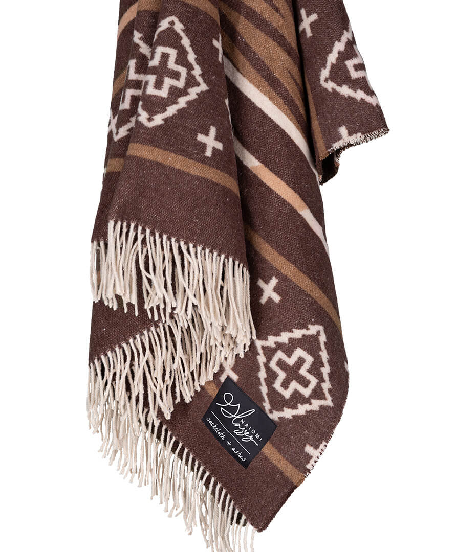 Brown patterned blanket with white fringes and a brand label on a white background