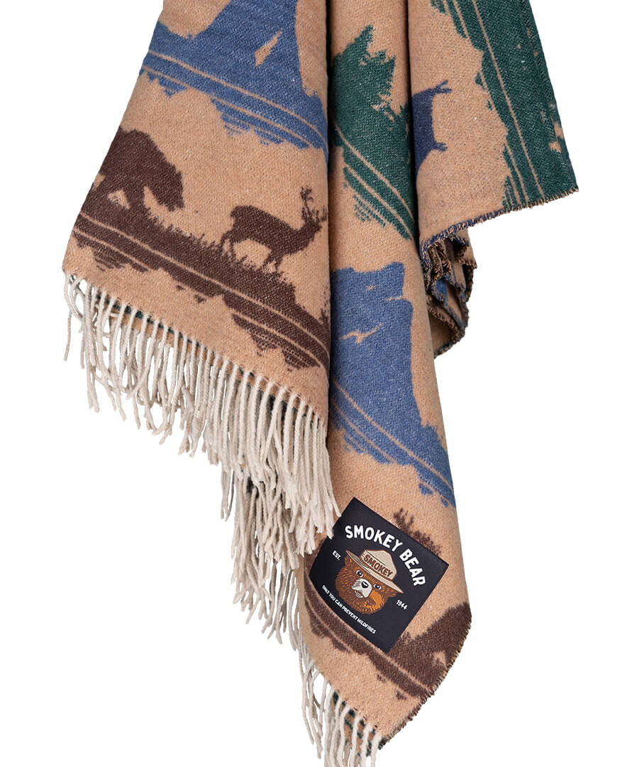 Woven blanket with nature-themed design featuring animals, branded 'Smokey Bear', on a white background.