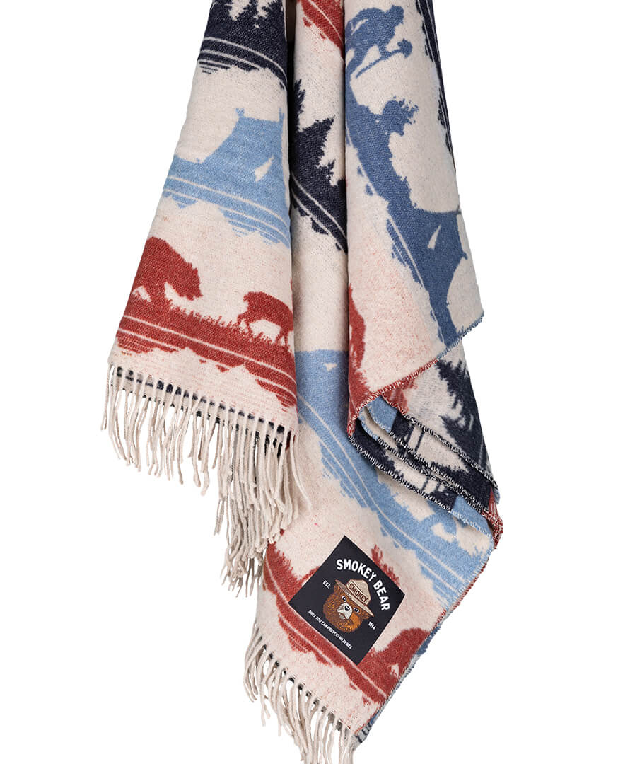 Woven blanket with outdoor scene design and Smokey Bear label on a white background