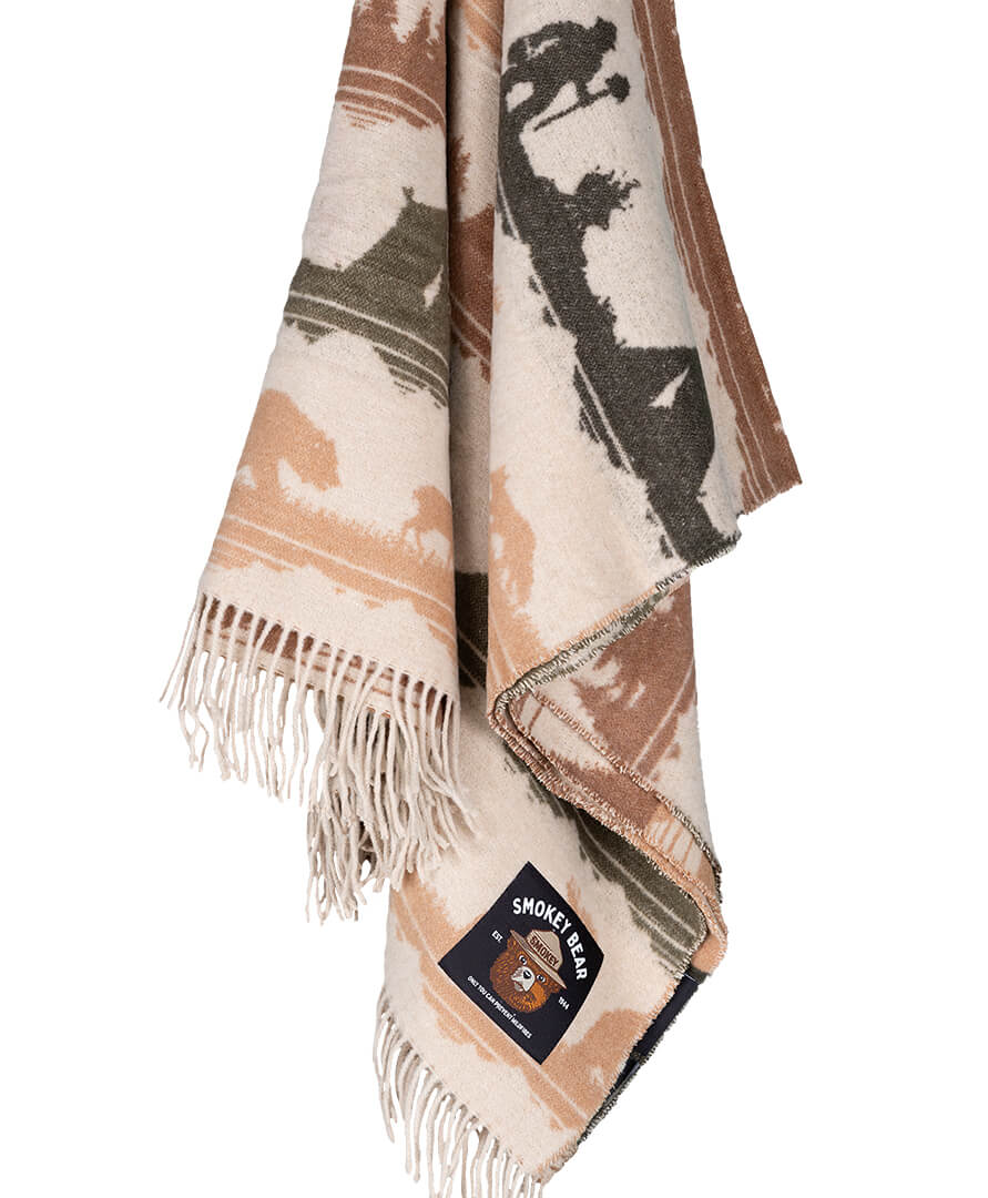 Folded blanket with nature-themed design and Smokey Bear logo on a white background