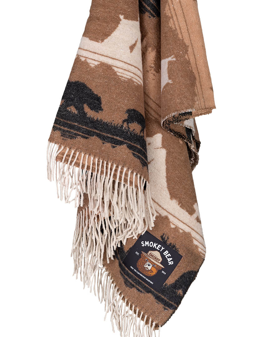 Brown and beige patterned blanket with fringes and Smokey Bear logo on a white background