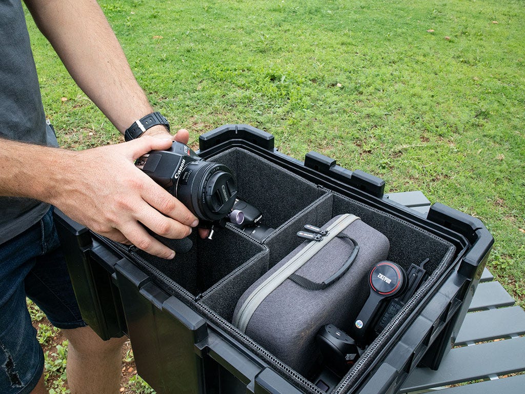 Person holding a camera over a black protective case with compartments on a grassy background