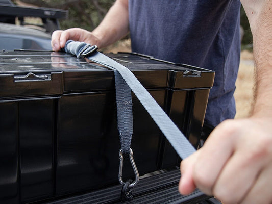 Person securing a black storage box with a strap in a vehicle's cargo area.